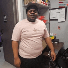 a man wearing a pink shirt and a black hat is standing in front of a desk .