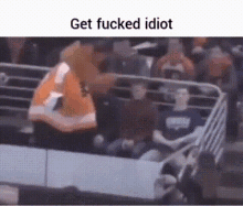 a group of people are sitting in a stadium with a sign that says get fucked idiot .