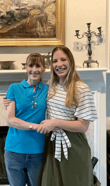 two women are posing for a picture in front of a painting