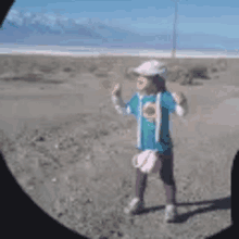 a little girl is standing in the middle of a desert wearing a hat .