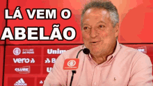 a man speaking into a microphone with the words " la vem o abelao " behind him