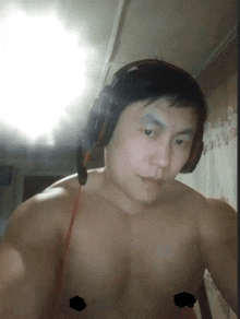 a shirtless man wearing headphones looks at the camera with a black square on his chest