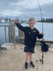 a young boy holding a fishing rod and wearing a nike hoodie