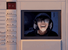 a man wearing glasses and a hood is smiling in front of a screen with a red button that says " bi " on it