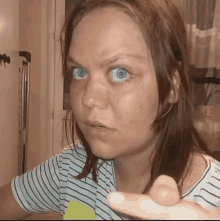 a woman with blue eyes and a striped shirt is making a funny face while holding a remote control .