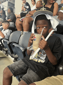 a young boy sitting in a stadium drinking from a pepsi cup