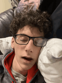 a young man wearing glasses is laying on a pillow