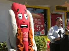 a man stands in front of a sign that says hot dogs