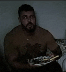 a shirtless man is holding a plate of food