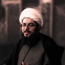 a man wearing glasses and a white turban looks at the camera