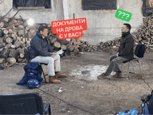 two men are sitting in front of a pile of logs and one has a sign that says " documents " on it