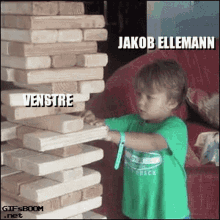 a young boy in a green shirt is playing with a stack of wooden blocks that says jakob ellemann on it