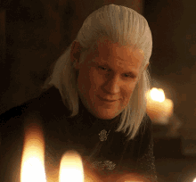 a man with long white hair is sitting in front of a candle