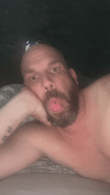 a shirtless man with a beard is laying on a bed with his tongue out