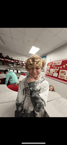 a boy wearing a sweatshirt that says tyrc is giving a peace sign in a classroom