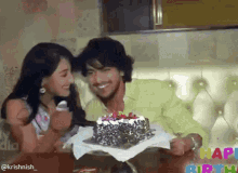 a man and a woman are sitting at a table with a birthday cake in front of them and a happy birthday sign