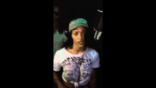 a woman wearing a hat and headphones stands in front of a microphone in a dark room