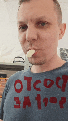 a man wearing a t-shirt that says " otcoy 3a 1op " is eating a piece of garlic