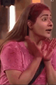 a woman in a pink shirt is making a surprised face with her hands outstretched .