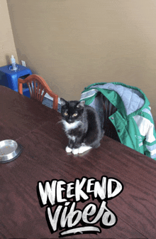 a black and white cat sits on a wooden table with the words weekend vibes written on it