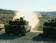 a couple of tanks are driving down a dirt road and one of them is firing a rocket .