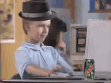 a boy wearing a top hat is sitting at a desk with a can of mountain dew in front of him .