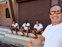 a man wearing sunglasses is giving a thumbs up next to three other men