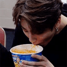 a man is eating noodles out of a cup .