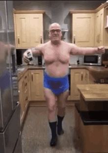 a man without a shirt is standing in a kitchen with his arms outstretched while holding a box .