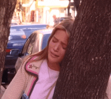 a woman leaning against a tree trunk with her eyes closed