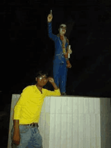 a man in a yellow shirt is standing next to a statue of a man