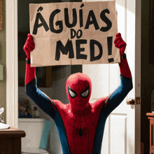 a man in a spiderman costume holds up a sign that says " aguias do med "