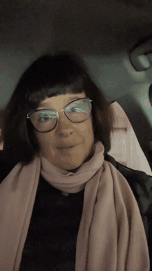 a woman wearing glasses and a pink scarf is sitting in the back seat of a car