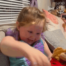 a little girl is sitting on a couch playing with a stuffed animal and the words happy little girl are visible in the background