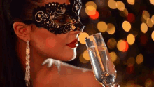 a woman wearing a masquerade mask is drinking from a glass of champagne .