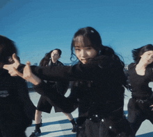 a group of women are dancing in front of a blue sky and the word open is on the back of their jacket