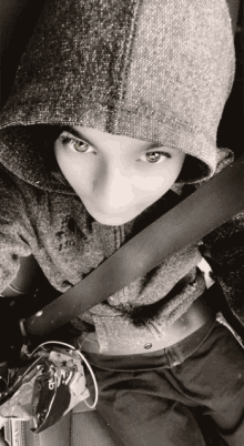 a woman wearing a hoodie and a seat belt looks at the camera in a black and white photo