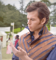 a man wearing a striped vest and a blue shirt is looking down