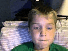 a young boy in a green shirt is making a funny face while laying in bed .