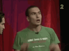 a man in a green t-shirt is standing on a stage talking to another man .