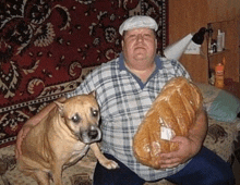 a man is holding a loaf of bread while a dog sits next to him