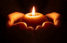 a person is holding a burning candle in their hands .