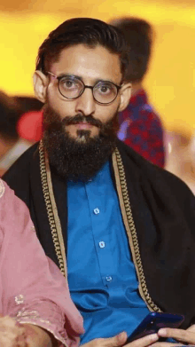 a man with glasses and a beard is wearing a blue shirt and a black shawl