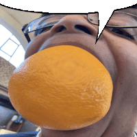 a man wearing glasses has an orange in his mouth