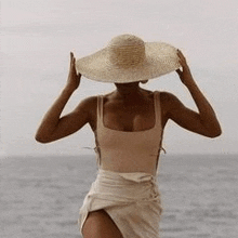 a woman in a swimsuit and straw hat is standing on a beach .