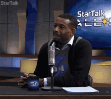 a man sitting in front of a microphone with a startalk all logo behind him