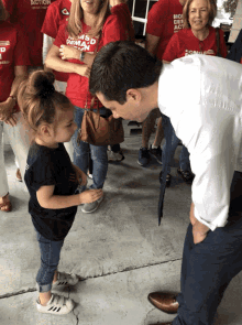 a man is talking to a little girl who is wearing a shirt that says " no more demagogs "