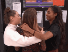 three women hugging each other in front of a bulletin board with papers on it including one that says ' french '