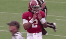 a football player wearing a red jersey with the number 2 on it is making a peace sign on the field .