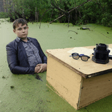 a man in a suit sits at a desk in the middle of a pond